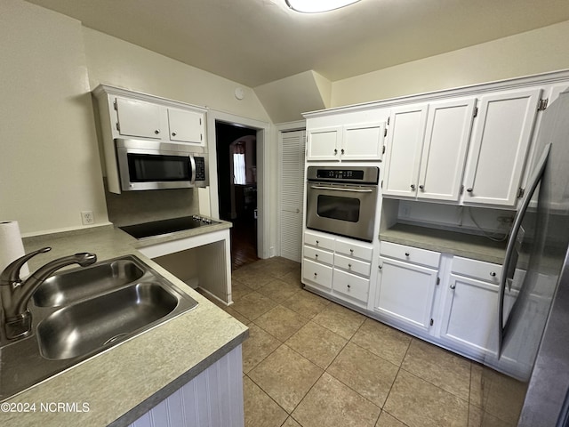 kitchen featuring stainless steel appliances, a sink, light tile patterned floors, white cabinets, and vaulted ceiling