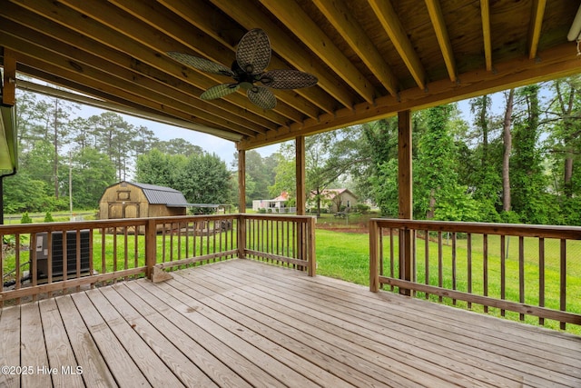 wooden deck featuring a storage unit, ceiling fan, view of wooded area, and an outdoor structure