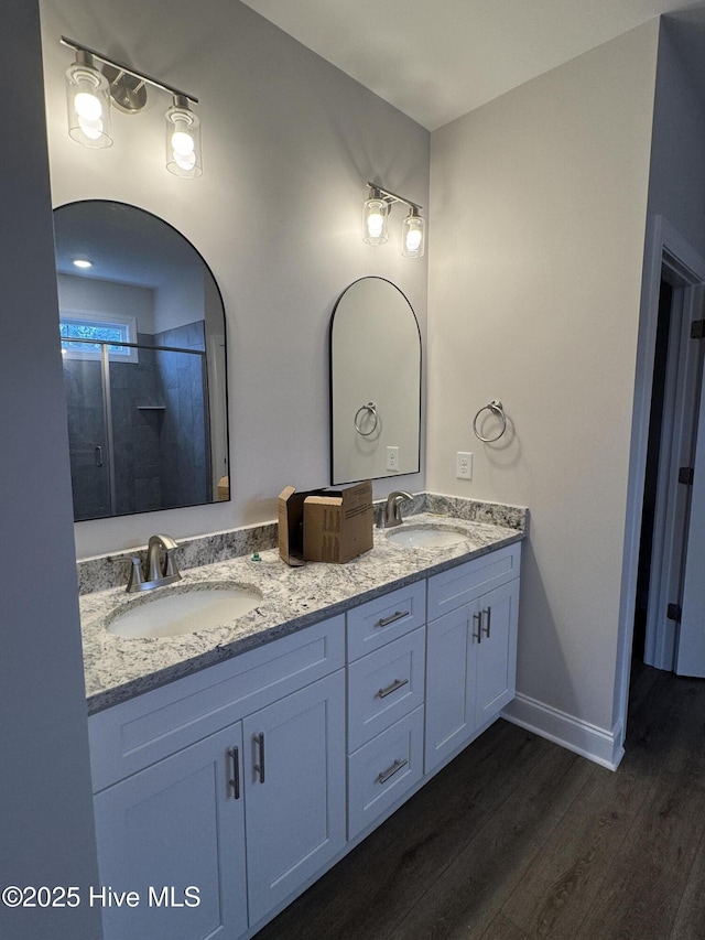 bathroom with wood finished floors, double vanity, baseboards, and a shower with door