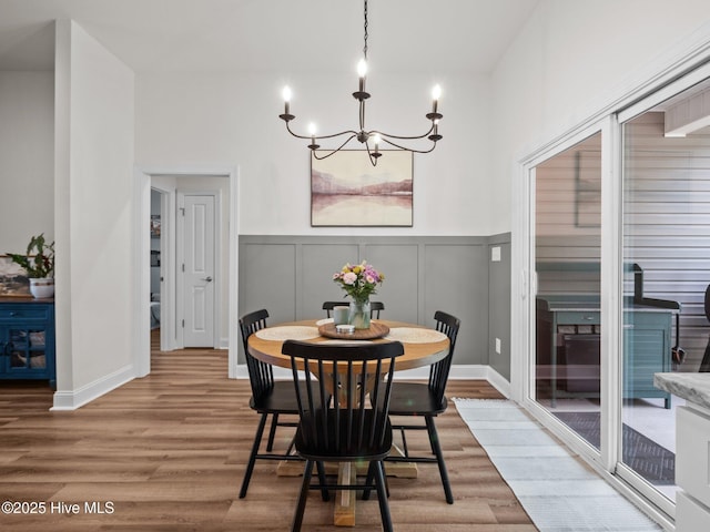 dining area featuring a chandelier, light wood finished floors, a decorative wall, and a wainscoted wall