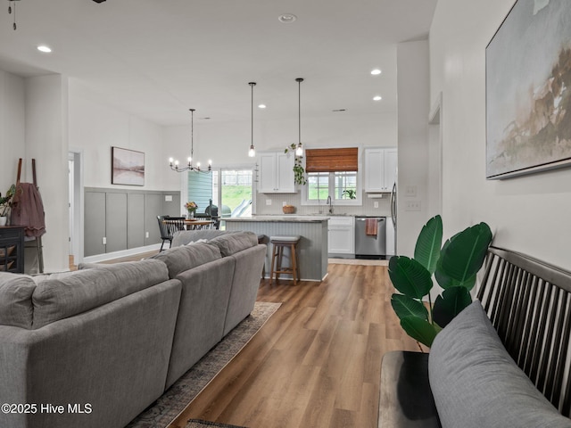 living room featuring light wood-type flooring, a chandelier, recessed lighting, and a wainscoted wall