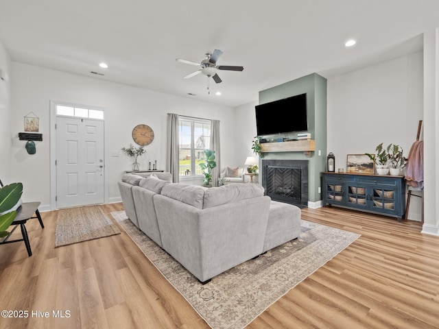living room featuring a fireplace with flush hearth, recessed lighting, light wood-type flooring, a ceiling fan, and baseboards