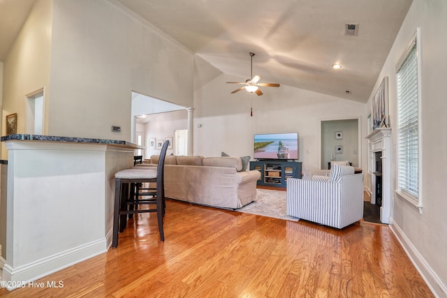 living area with light wood-style floors, ceiling fan, vaulted ceiling, a fireplace, and baseboards