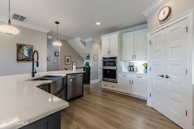 kitchen featuring stainless steel appliances, crown molding, white cabinetry, decorative light fixtures, and tasteful backsplash