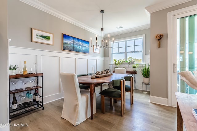dining room featuring a chandelier, crown molding, a decorative wall, light wood finished floors, and wainscoting