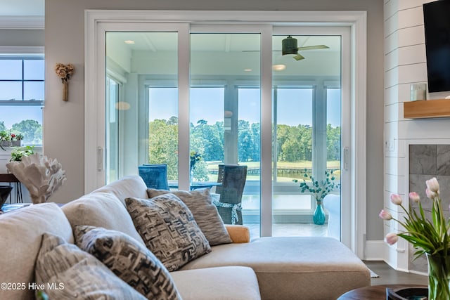 living area with ceiling fan, wood finished floors, a glass covered fireplace, and baseboards