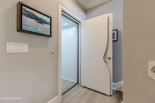 corridor with light wood-type flooring, crown molding, and baseboards