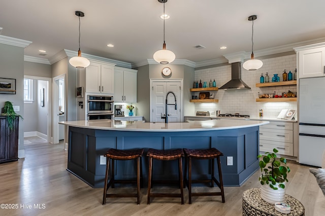 kitchen with wall chimney range hood, open shelves, light countertops, stainless steel appliances, and tasteful backsplash