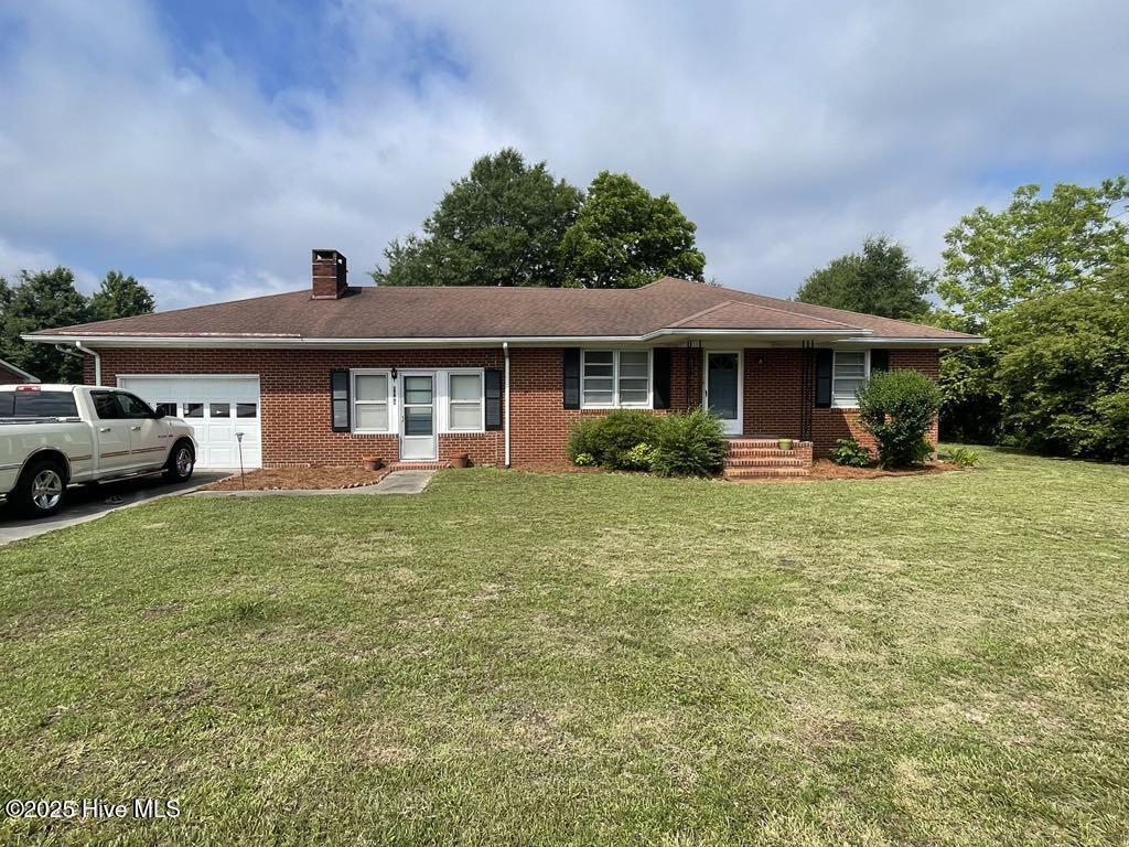 single story home featuring an attached garage, brick siding, a front lawn, and a chimney