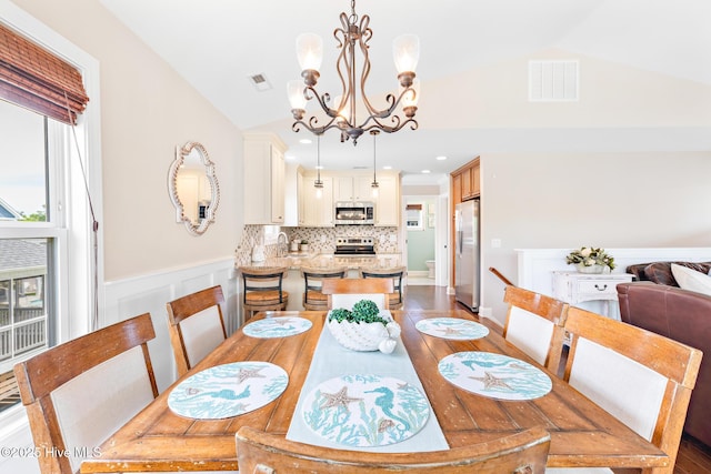 104 SE 32nd St, Oak Island, NC 28465 - dining space with vaulted ceiling, a chandelier, a wainscoted wall, and wood finished floors