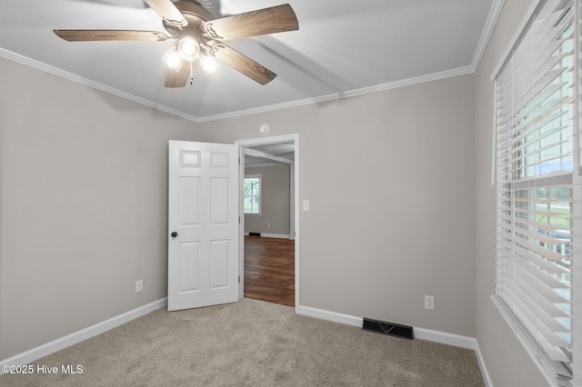 carpeted empty room with ornamental molding, a ceiling fan, and baseboards