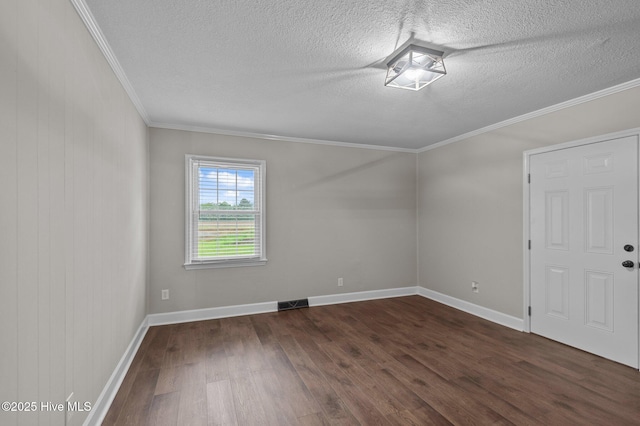 empty room with dark wood finished floors, a textured ceiling, ornamental molding, and baseboards