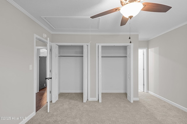 unfurnished bedroom featuring attic access, multiple closets, light carpet, ornamental molding, and ceiling fan
