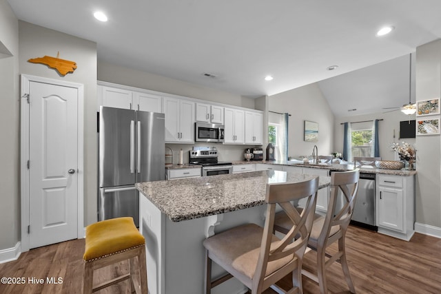 kitchen with appliances with stainless steel finishes, dark wood-style flooring, a kitchen island, white cabinets, and vaulted ceiling