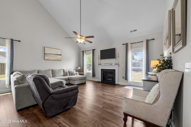 living room featuring wood finished floors, high vaulted ceiling, healthy amount of natural light, a fireplace with flush hearth, and a ceiling fan