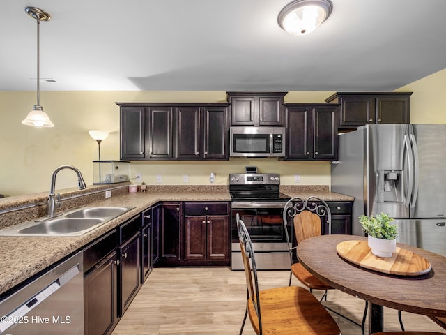 kitchen featuring stainless steel appliances, a sink, hanging light fixtures, light wood-style flooring, and a peninsula