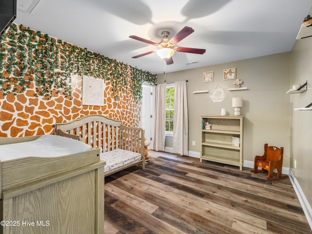 bedroom featuring wood finished floors, baseboards, ceiling fan, and an accent wall