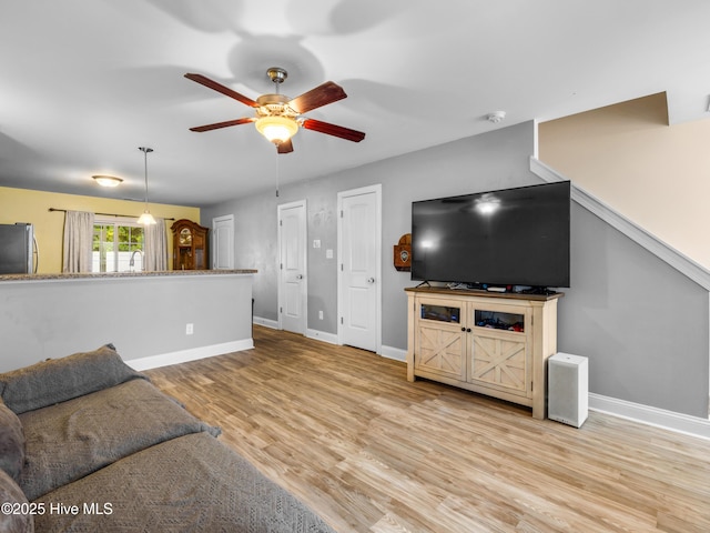 unfurnished living room with a ceiling fan, baseboards, light wood-style floors, and a sink