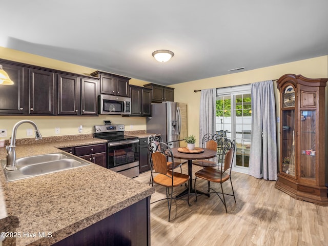 kitchen with appliances with stainless steel finishes, a sink, dark brown cabinetry, and light wood finished floors