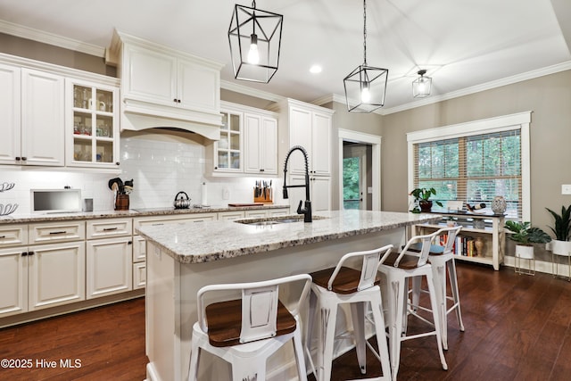 kitchen featuring a sink, dark wood finished floors, light stone countertops, decorative backsplash, and an island with sink