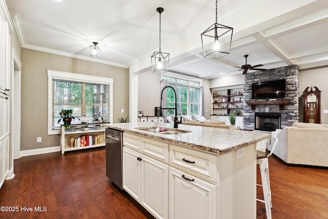kitchen with a sink, dishwasher, ceiling fan, a stone fireplace, and dark wood-style flooring