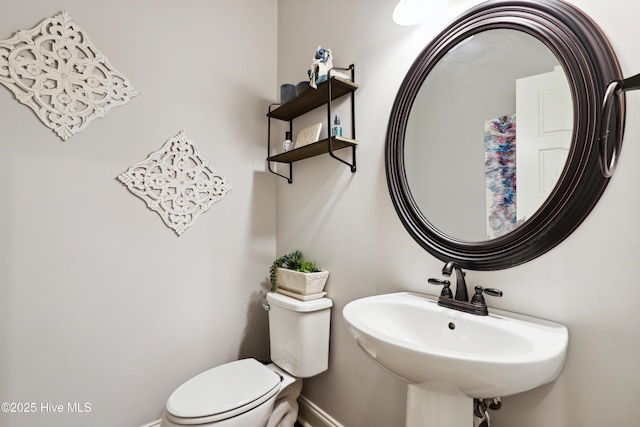 half bath with baseboards, toilet, and a sink