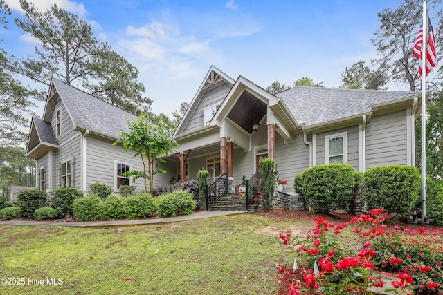 view of front of house with a porch, a front yard, and roof with shingles