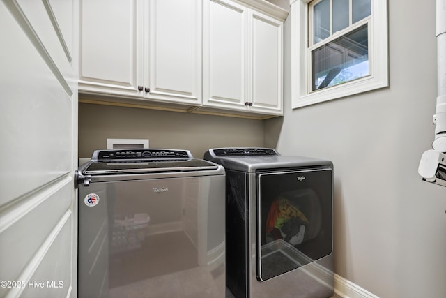 washroom featuring separate washer and dryer, cabinet space, and baseboards