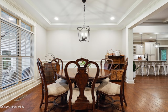dining space with a raised ceiling, dark wood-style flooring, ornamental molding, and a chandelier