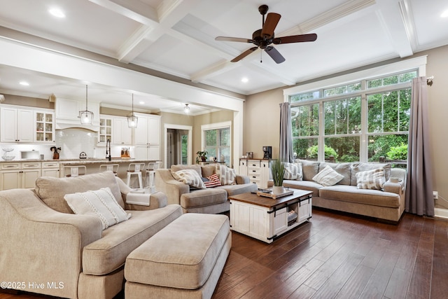 living area with a ceiling fan, beam ceiling, coffered ceiling, dark wood-style flooring, and ornamental molding
