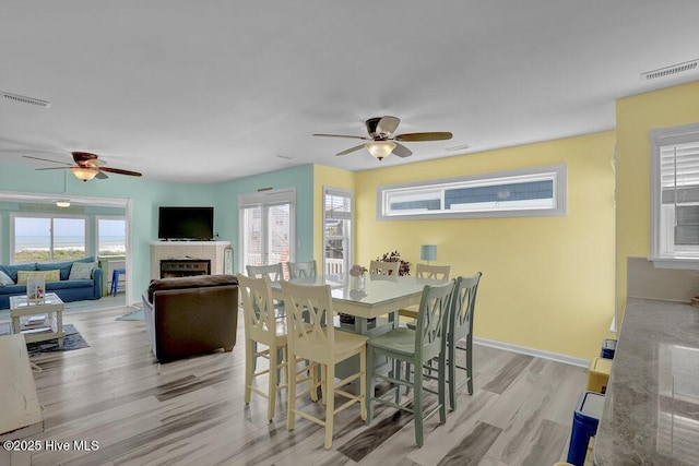 dining room with a ceiling fan, a tile fireplace, light wood finished floors, and healthy amount of natural light
