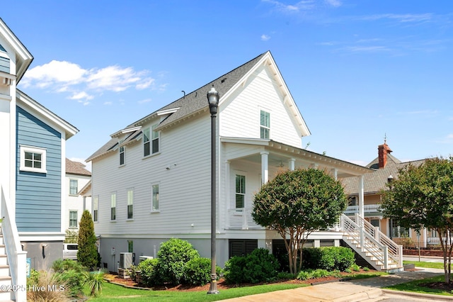 view of side of property featuring cooling unit, stairs, and roof with shingles