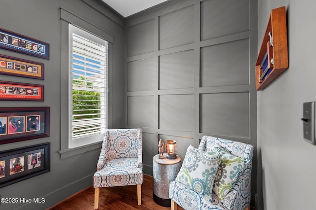sitting room featuring a decorative wall, wood finished floors, and baseboards