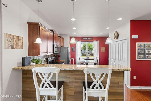 4007 Norseman Loop Unit 5, Southport, NC 28461 - kitchen featuring appliances with stainless steel finishes, light stone counters, a peninsula, wood finished floors, and pendant lighting