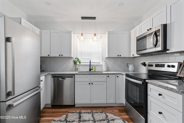 kitchen with appliances with stainless steel finishes, a sink, decorative backsplash, light wood-type flooring, and light stone countertops