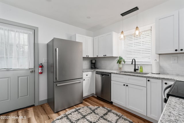 kitchen with appliances with stainless steel finishes, a sink, backsplash, white cabinets, and light wood-type flooring