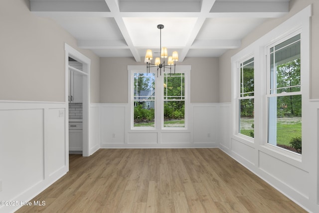 unfurnished dining area featuring a chandelier, plenty of natural light, coffered ceiling, a decorative wall, and light wood-type flooring