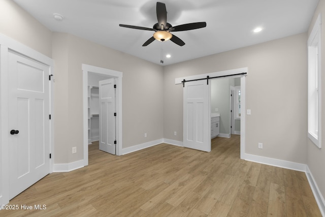 unfurnished bedroom featuring a spacious closet, a barn door, light wood-style floors, baseboards, and recessed lighting