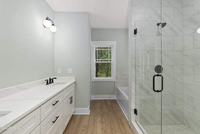 full bathroom with wood finished floors, a shower stall, a garden tub, double vanity, and baseboards