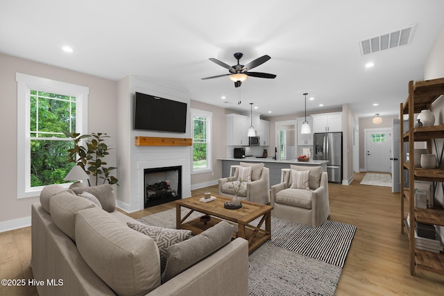 living area featuring baseboards, light wood-type flooring, ceiling fan, a fireplace, and recessed lighting