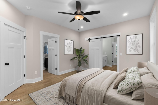 bedroom featuring a barn door, a walk in closet, light wood finished floors, baseboards, and recessed lighting