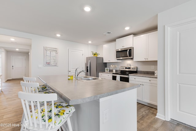 kitchen featuring appliances with stainless steel finishes, a sink, a kitchen breakfast bar, a kitchen island with sink, and light wood-style flooring