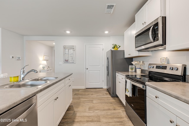 kitchen with stainless steel appliances, a sink, white cabinetry, light wood-style floors, and recessed lighting