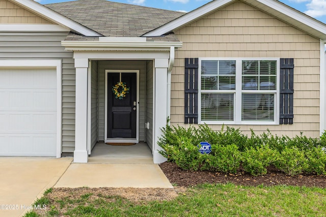 doorway to property with an attached garage and roof with shingles