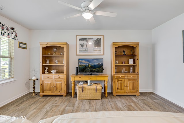 living area with light wood-style flooring, a ceiling fan, and baseboards