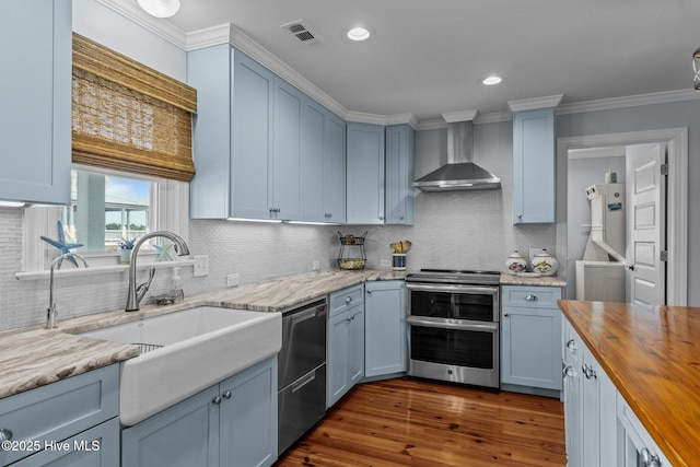 141 Bayview Blvd, Atlantic Beach, NC 28512 - kitchen featuring appliances with stainless steel finishes, wall chimney range hood, butcher block countertops, a sink, and blue cabinets