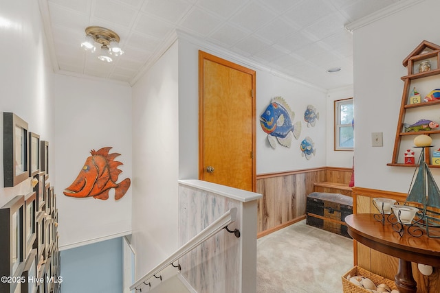 hallway featuring a wainscoted wall, light colored carpet, an upstairs landing, wooden walls, and ornamental molding