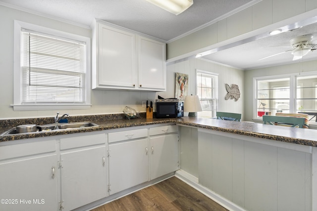 kitchen with crown molding, black microwave, a sink, dark wood-type flooring, and white cabinetry