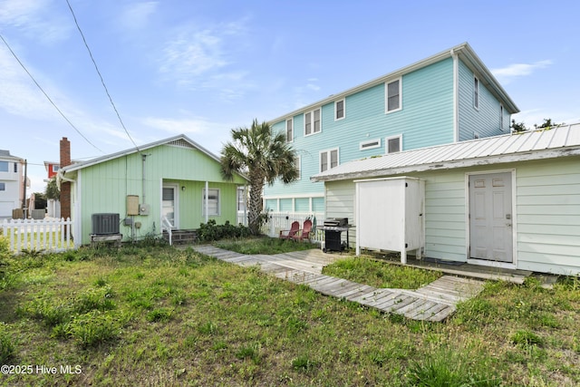 rear view of house featuring fence, central AC, and metal roof