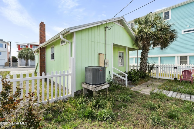 rear view of property with central air condition unit, fence, and a chimney